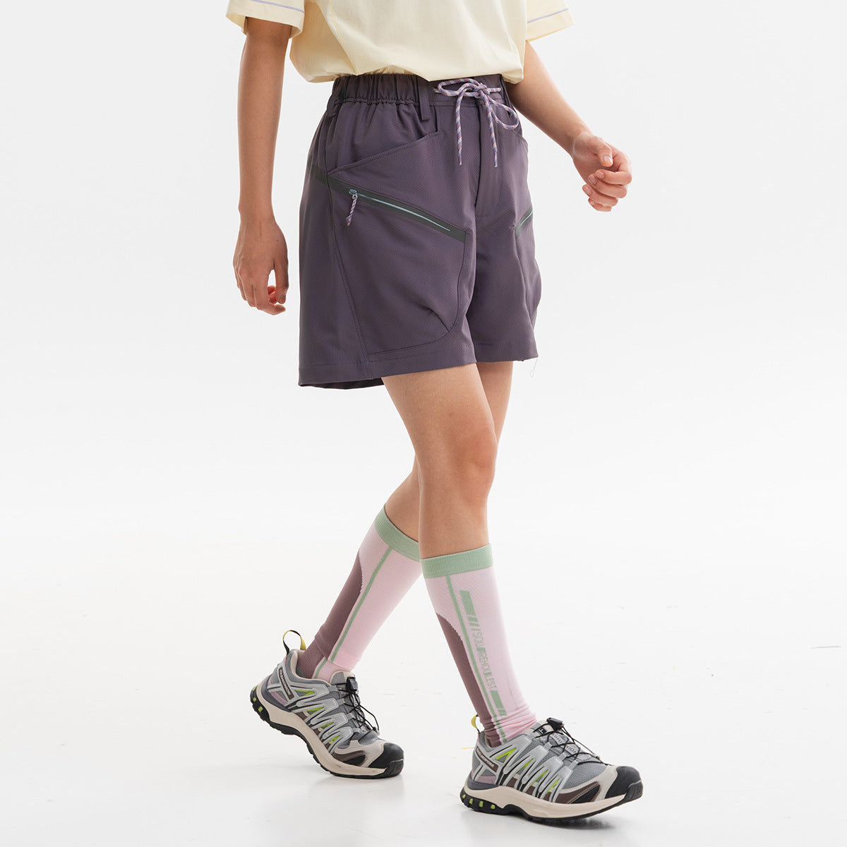Model wearing dark plum shorts with an elastic drawstring waist and large angled zip pockets, shown from the side.