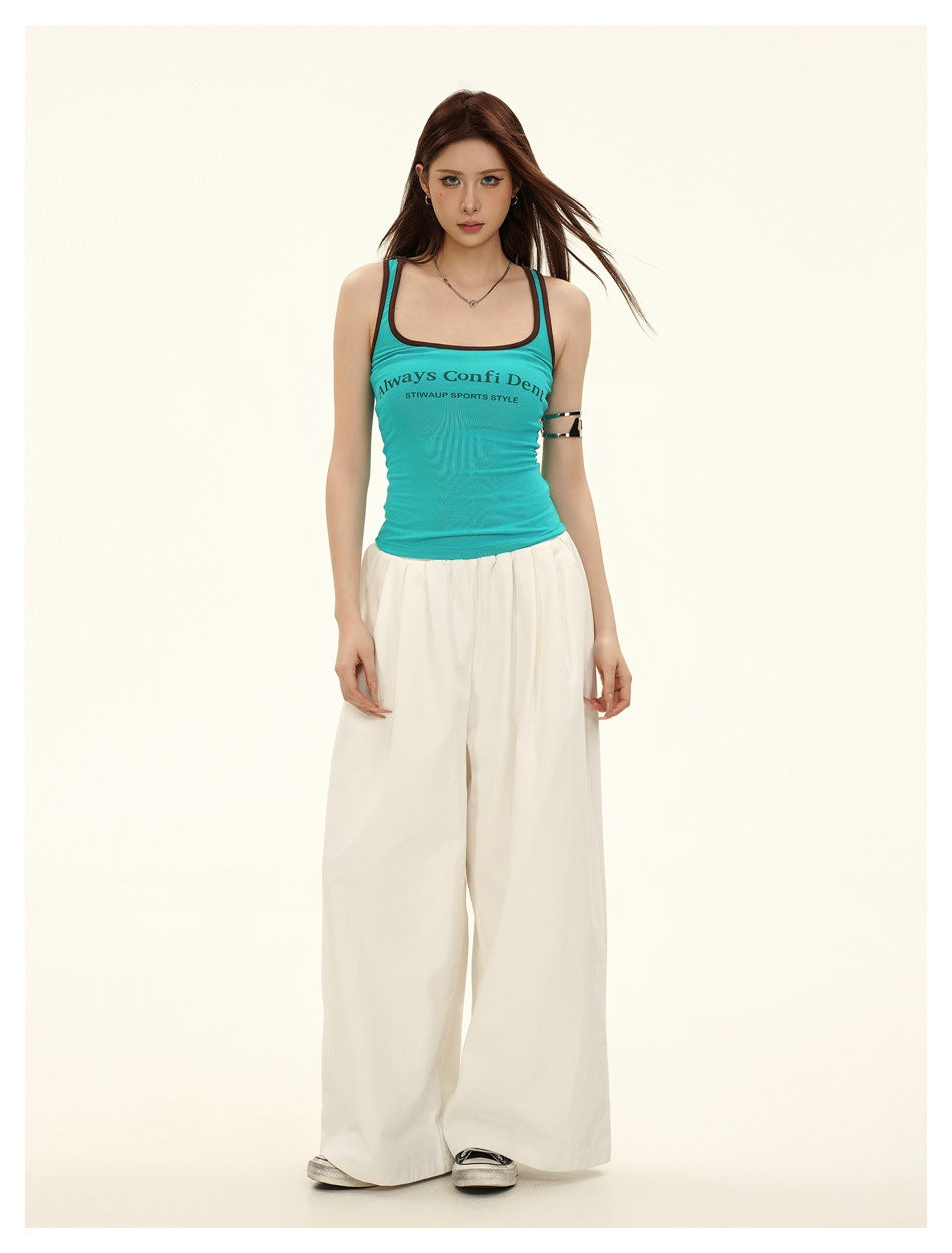 Model wearing lake blue scoop-neck tank top with brown trim and chest print, styled with wide-leg white pants