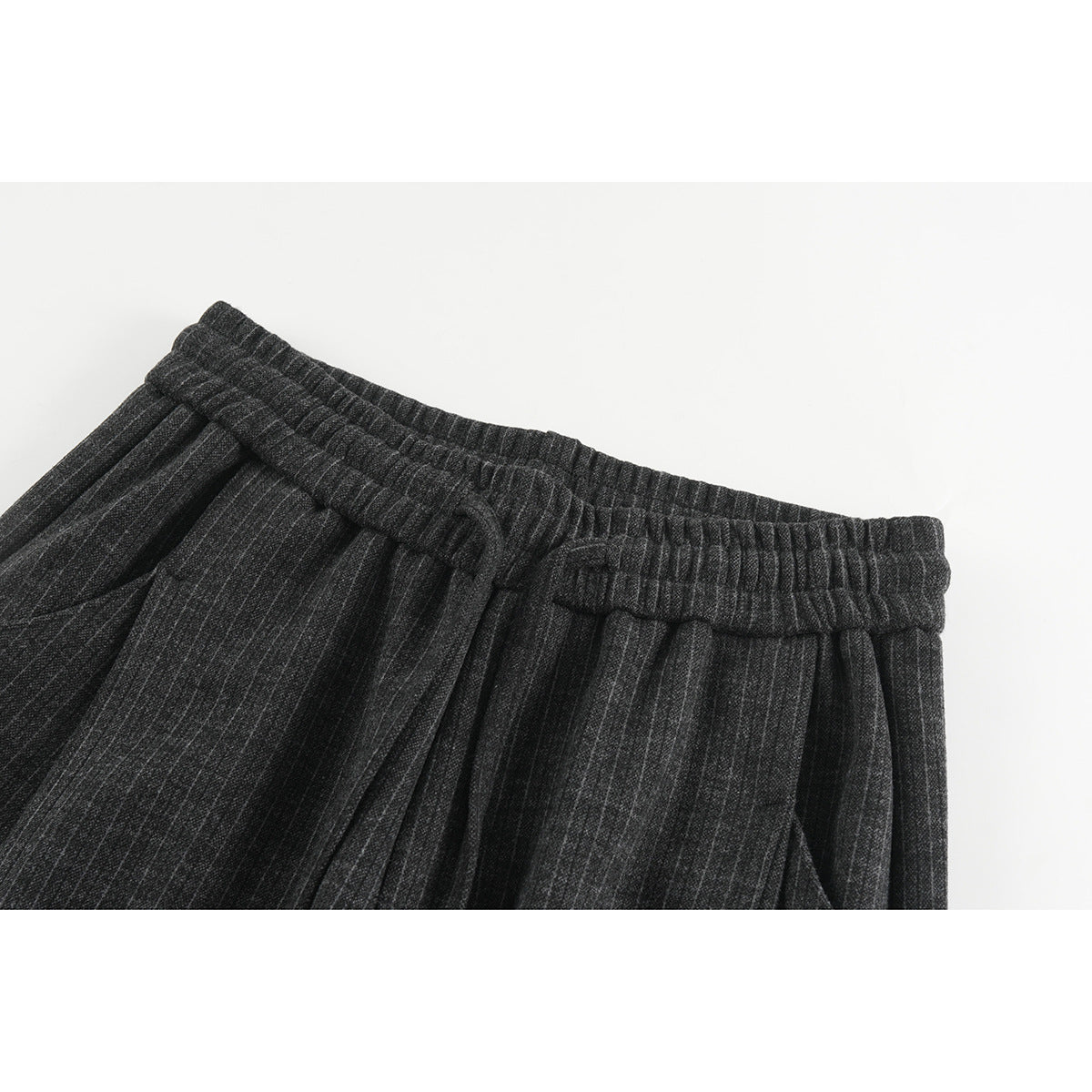 Close-up of charcoal pinstripe trousers showing the gathered elastic waistband, pleats, and front drawstring.