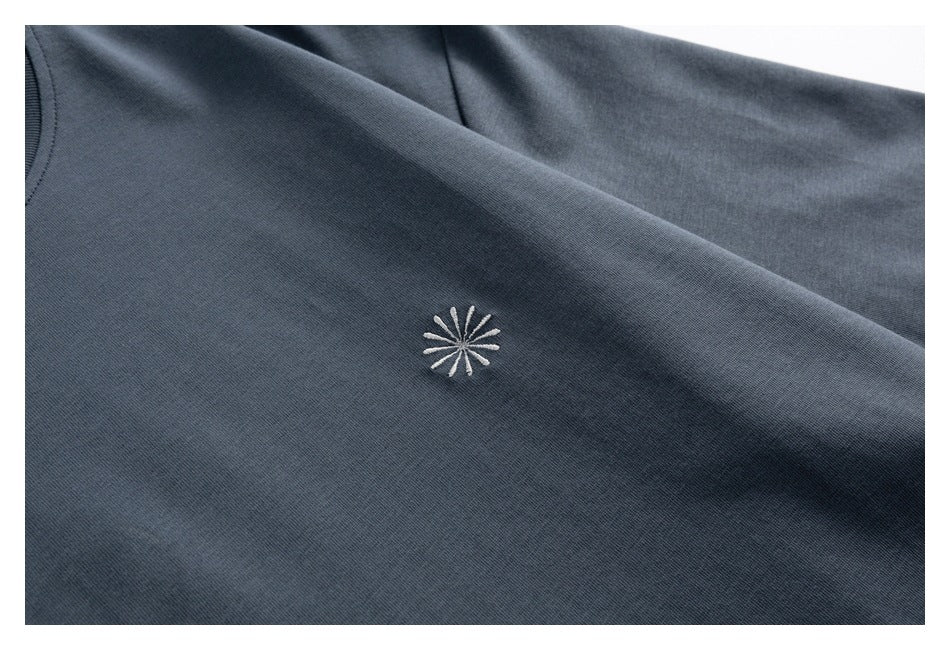 Close-up of a small white embroidered starburst on dark slate-gray fabric.