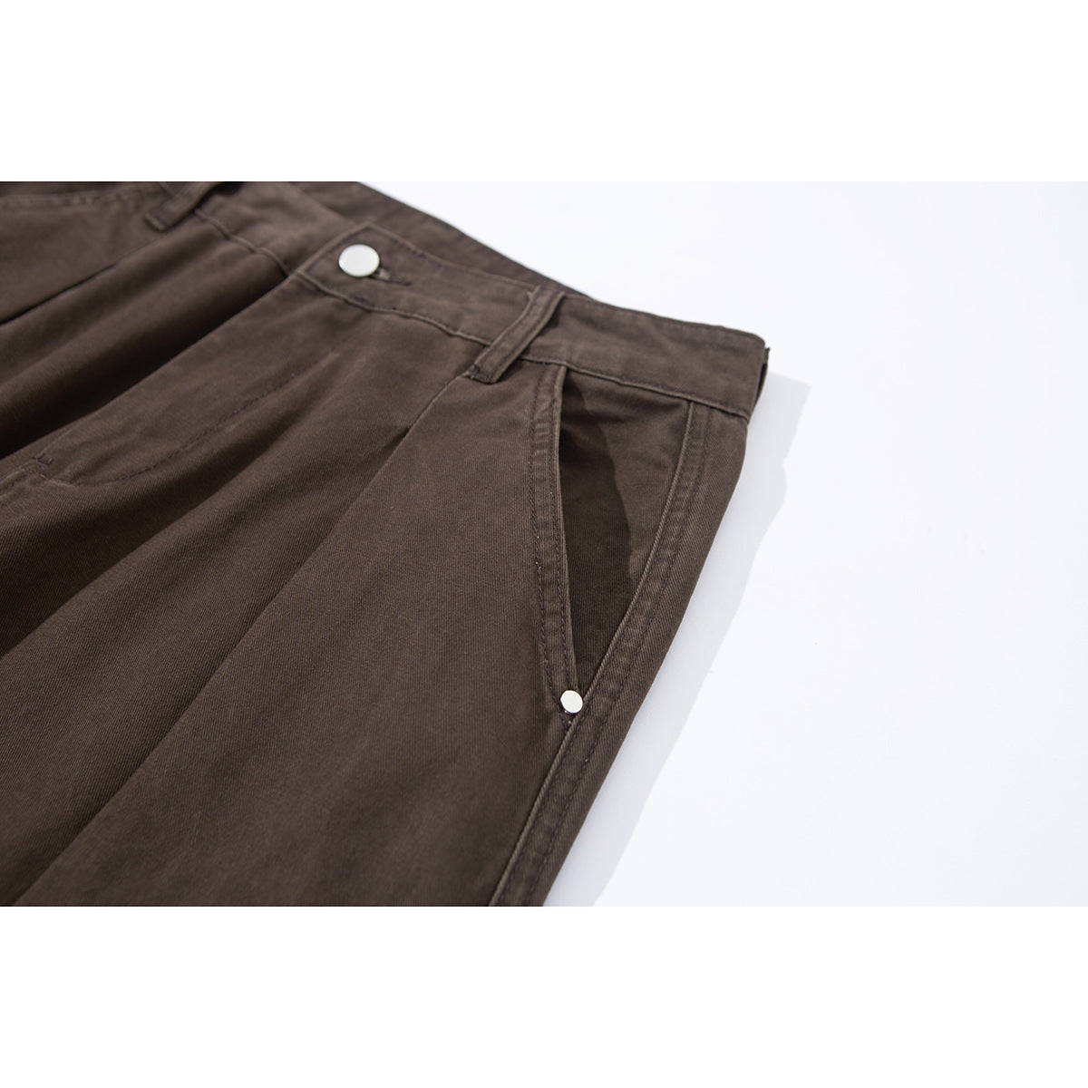 Angled close-up of dark brown cargo pants showing a front pleat, waistband button and side pocket with a metal stud.