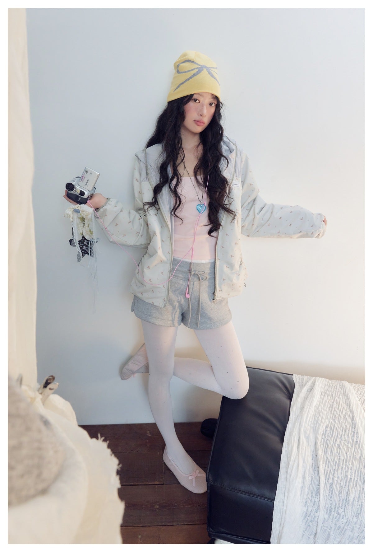 Full-body outfit view featuring a pale floral zip jacket, gray shorts, white tights and yellow beanie.