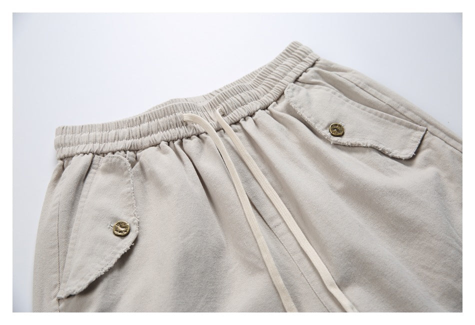 Close-up of the beige pants' elastic waistband, drawstrings and flap pockets with brass-tone buttons.