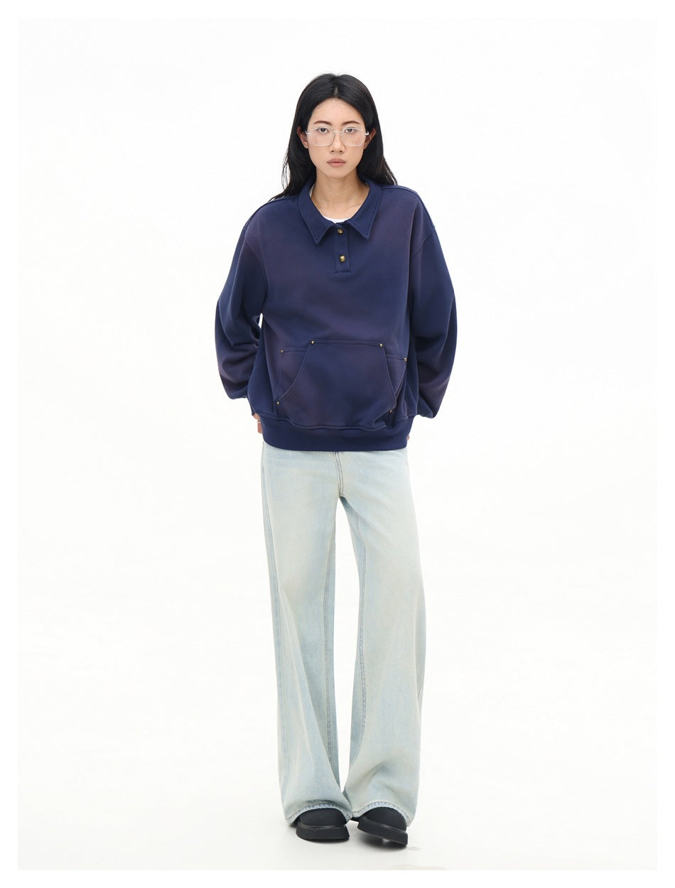 Full-length front view of a model wearing a navy collared sweatshirt with a studded front pocket and pale wide-leg jeans.
