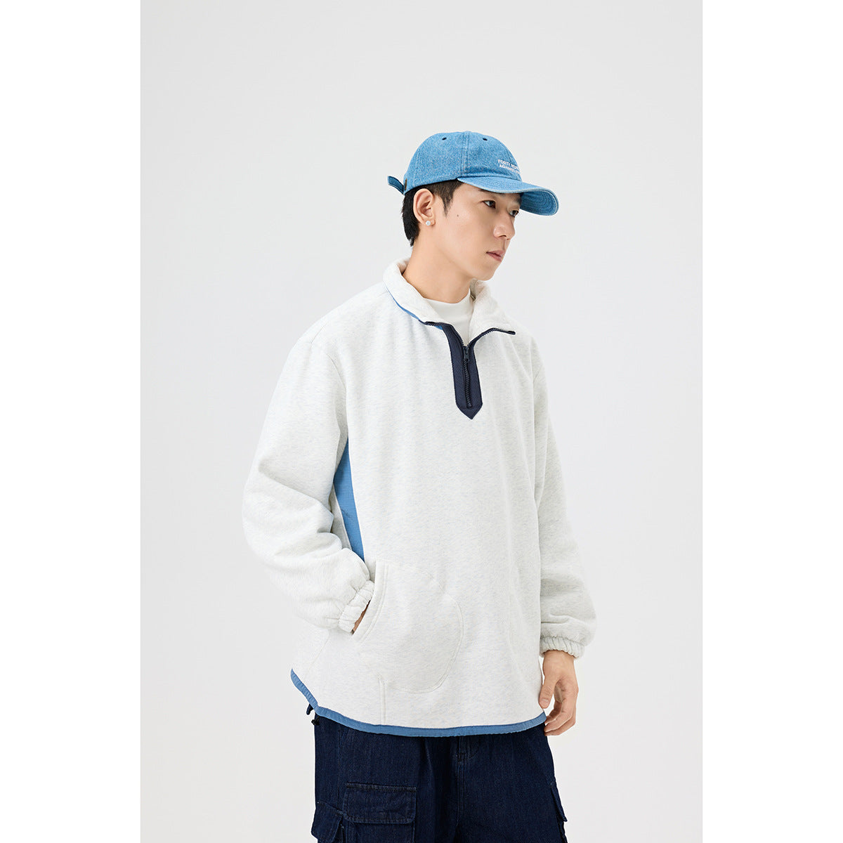 Three-quarter view of a man wearing a light gray pullover with a blue collar and side panels, navy quarter zip, and front