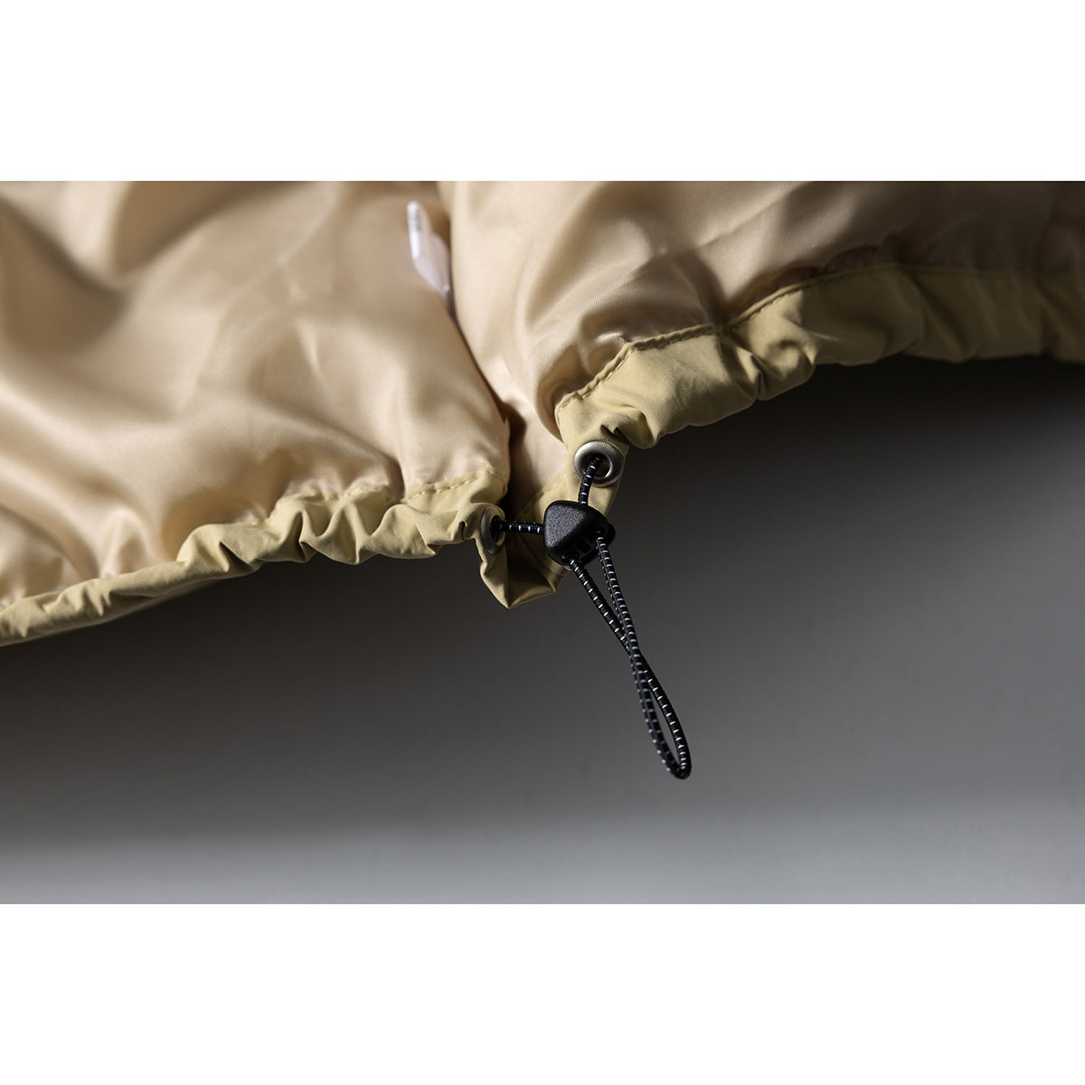 Close-up of a beige jacket's adjustable hem drawcord and toggle.