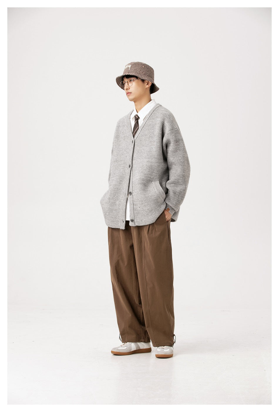 Model wearing light gray waffle-knit cardigan open over a white shirt and tie with brown wide pants