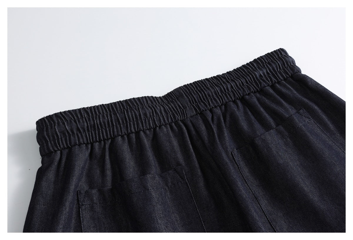 Close-up of dark indigo trousers showing a gathered elastic waistband and front pleats.