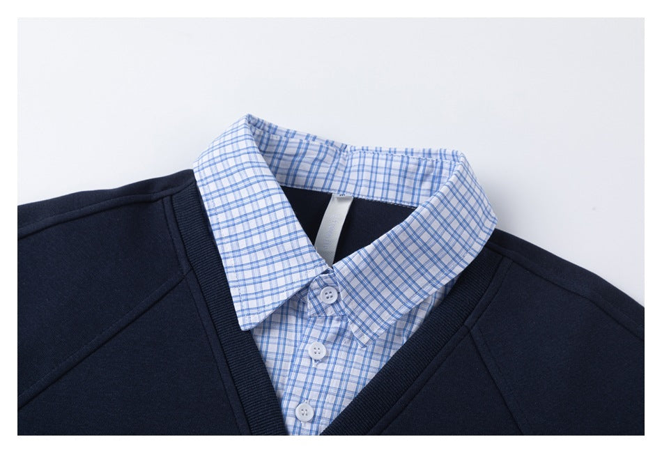 Close-up of the navy V-neck sweatshirt layered over a blue checked shirt with a pointed collar and white buttons.