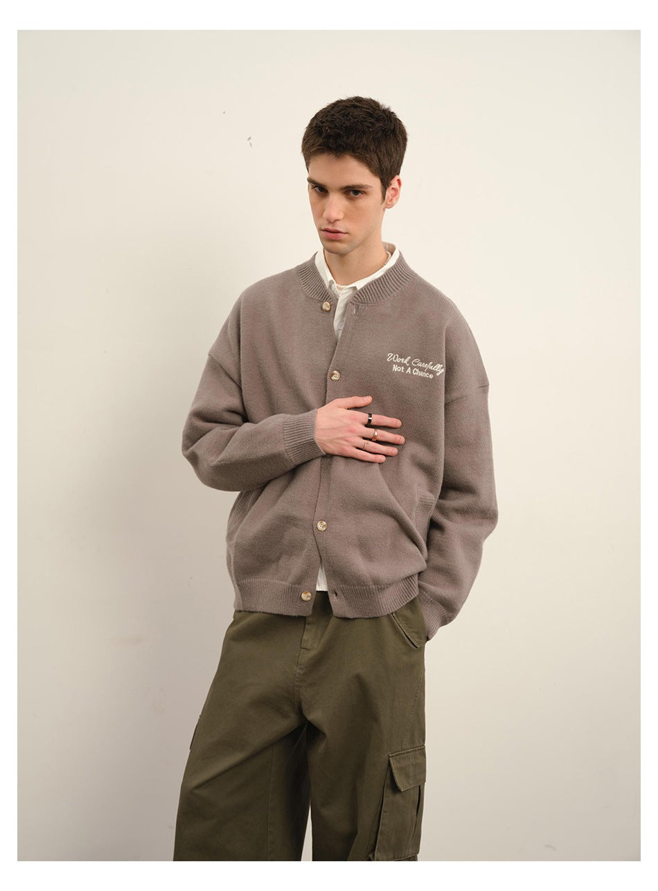 Closer view of a model wearing a taupe button-front cardigan with embroidered chest text and olive cargo trousers.