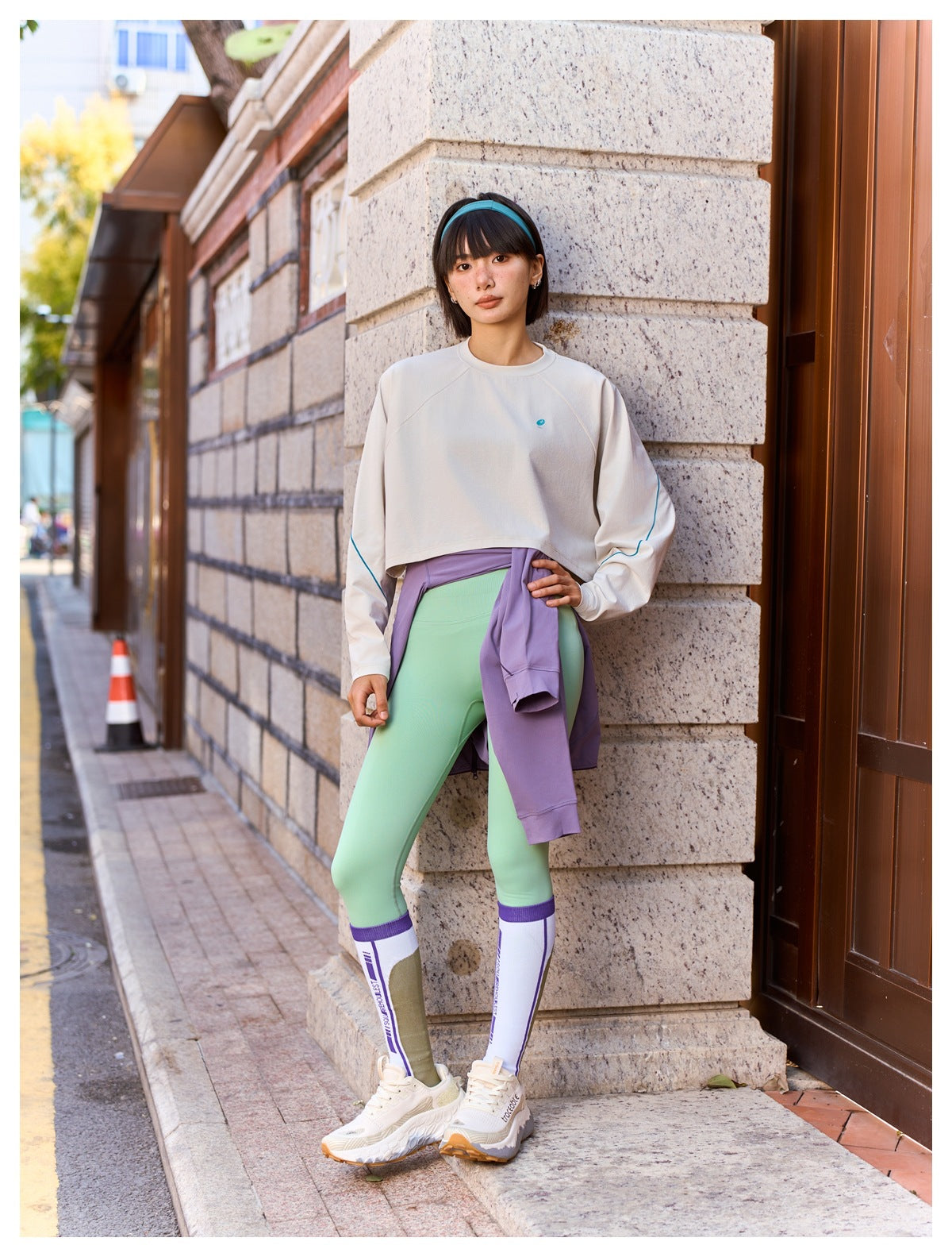 Model wearing a pale cream cropped long-sleeve top with blue sleeve piping and mint leggings on a city street.