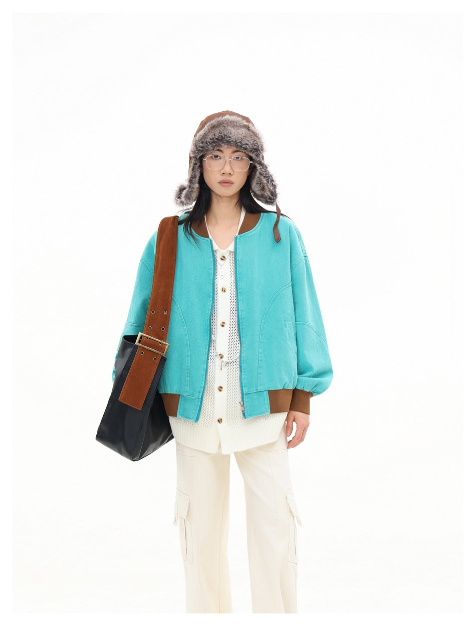 Front view of a model wearing a turquoise bomber jacket with brown trim over a cream cardigan.