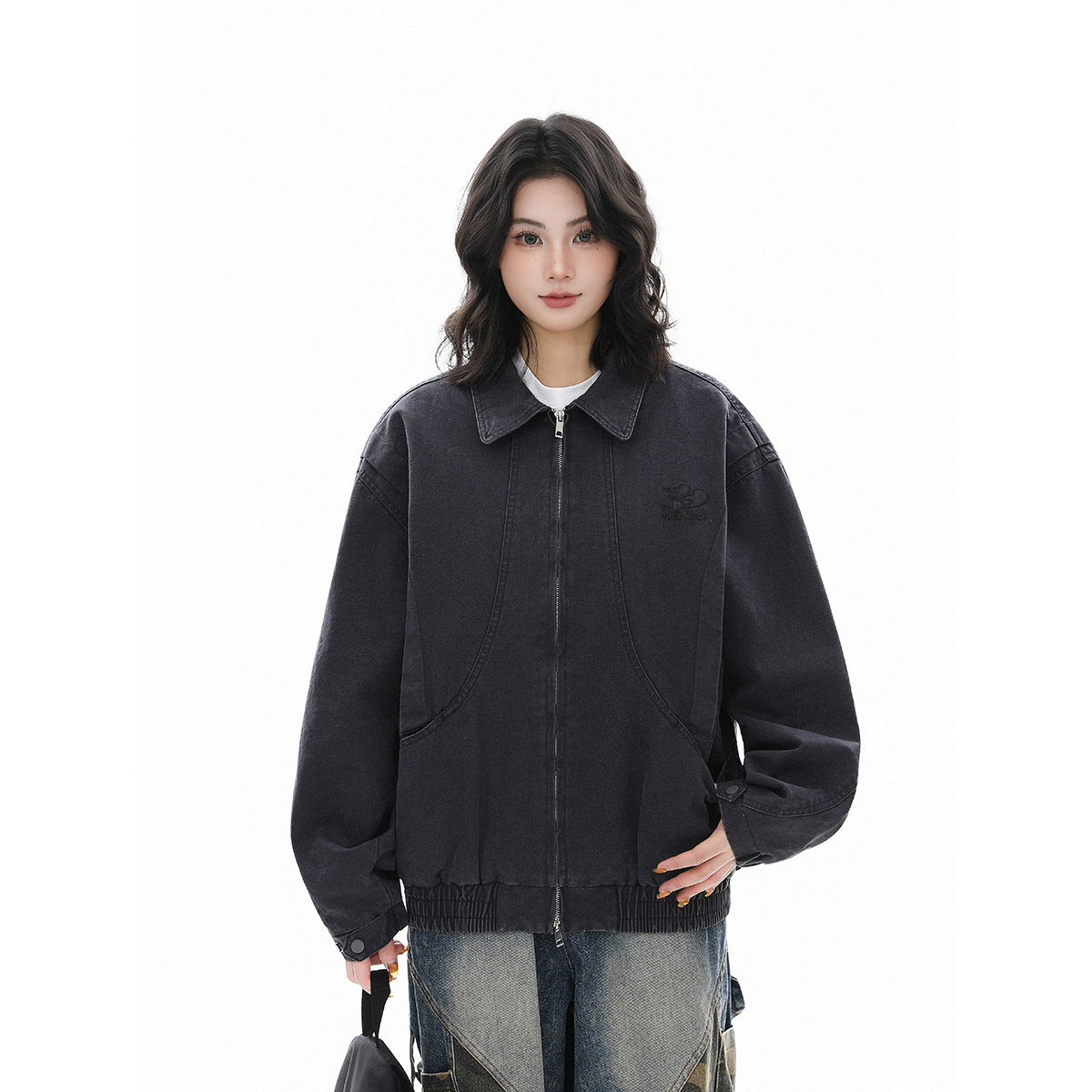 Model wearing a charcoal zip-front jacket with a pointed collar, curved pockets, gathered hem, and oversized sleeves.