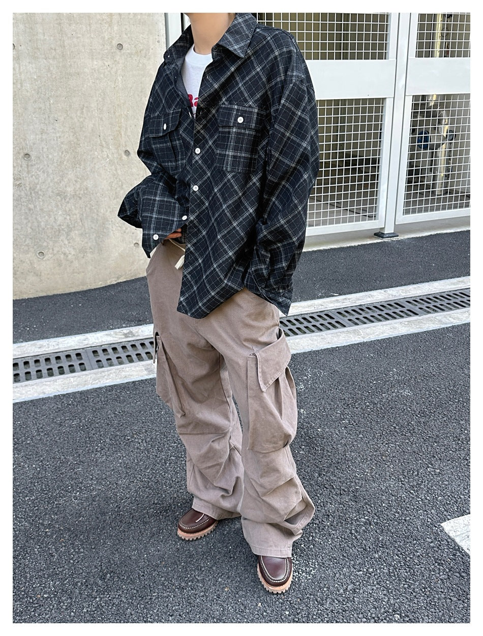 Cropped model wearing an oversized dark plaid button-up shirt and loose taupe cargo trousers.