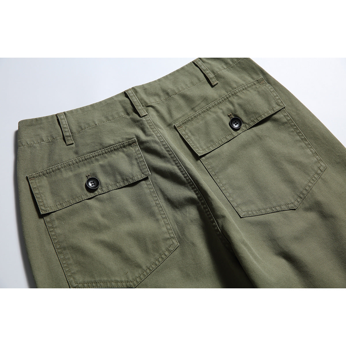 Close-up of olive-green trousers showing two button-flap back pockets and belt loops.