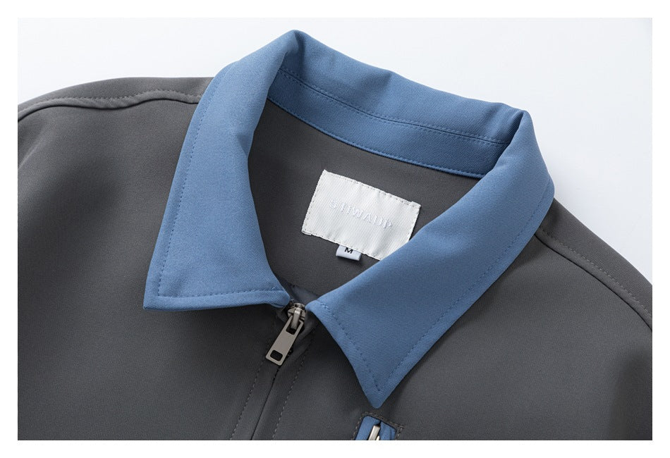 Close-up of a charcoal jacket with a blue pointed collar, front zipper, and white neck label.