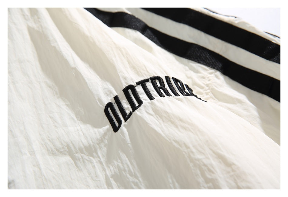 Close-up of black embroidered lettering and a black stripe on a crinkled ivory garment.