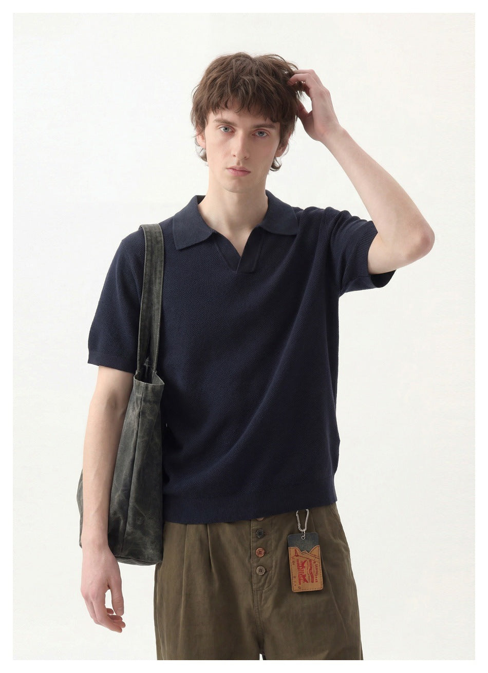 Model wearing a dark navy short-sleeve polo with a notched collar and olive-brown trousers.