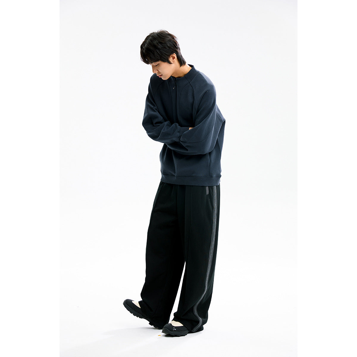 Three-quarter view of a model in a dark navy high-neck pullover and black wide-leg pants, arms folded.