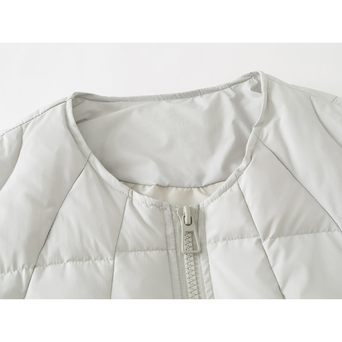Close-up of an ivory quilted vest's round neckline and front zipper.