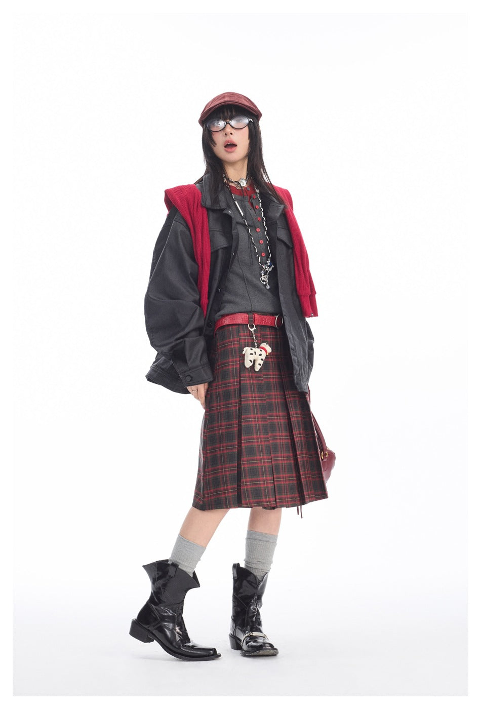 Model in open oversized black coated jacket over gray henley top, plaid skirt, red sweater and black boots