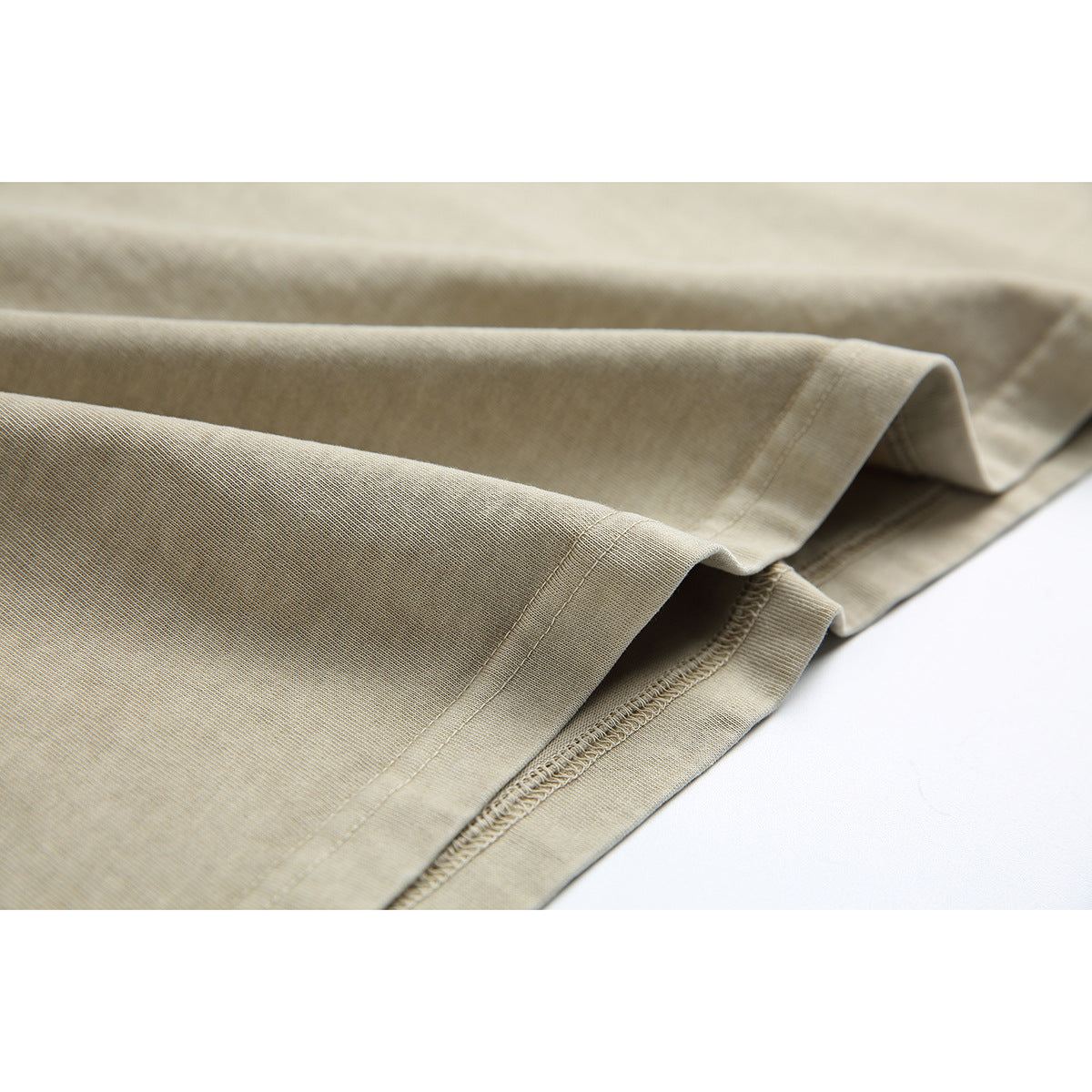 Close-up of the beige T-shirt’s folded hem and visible stitching.