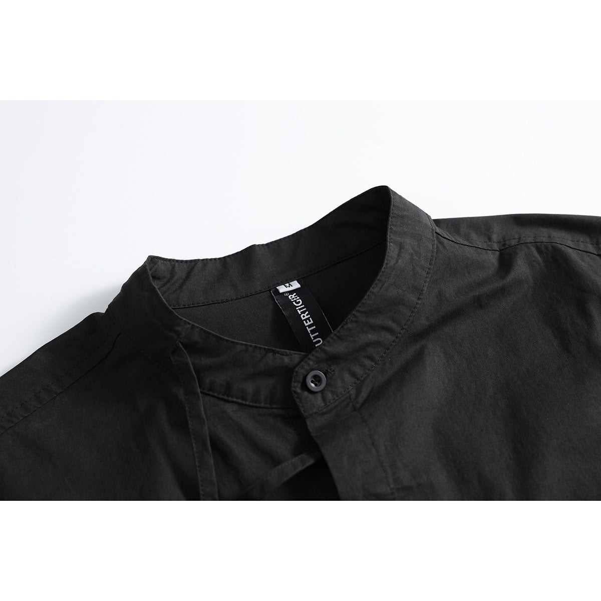Close-up of a black shirt's band collar, button, stitching, and inner neck label.