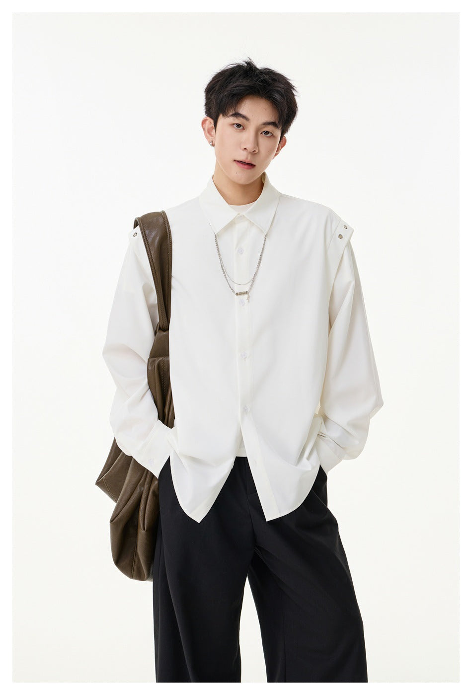 Model wearing an oversized white button-up shirt with snap-tab shoulders and a chain necklace, paired with black trousers.