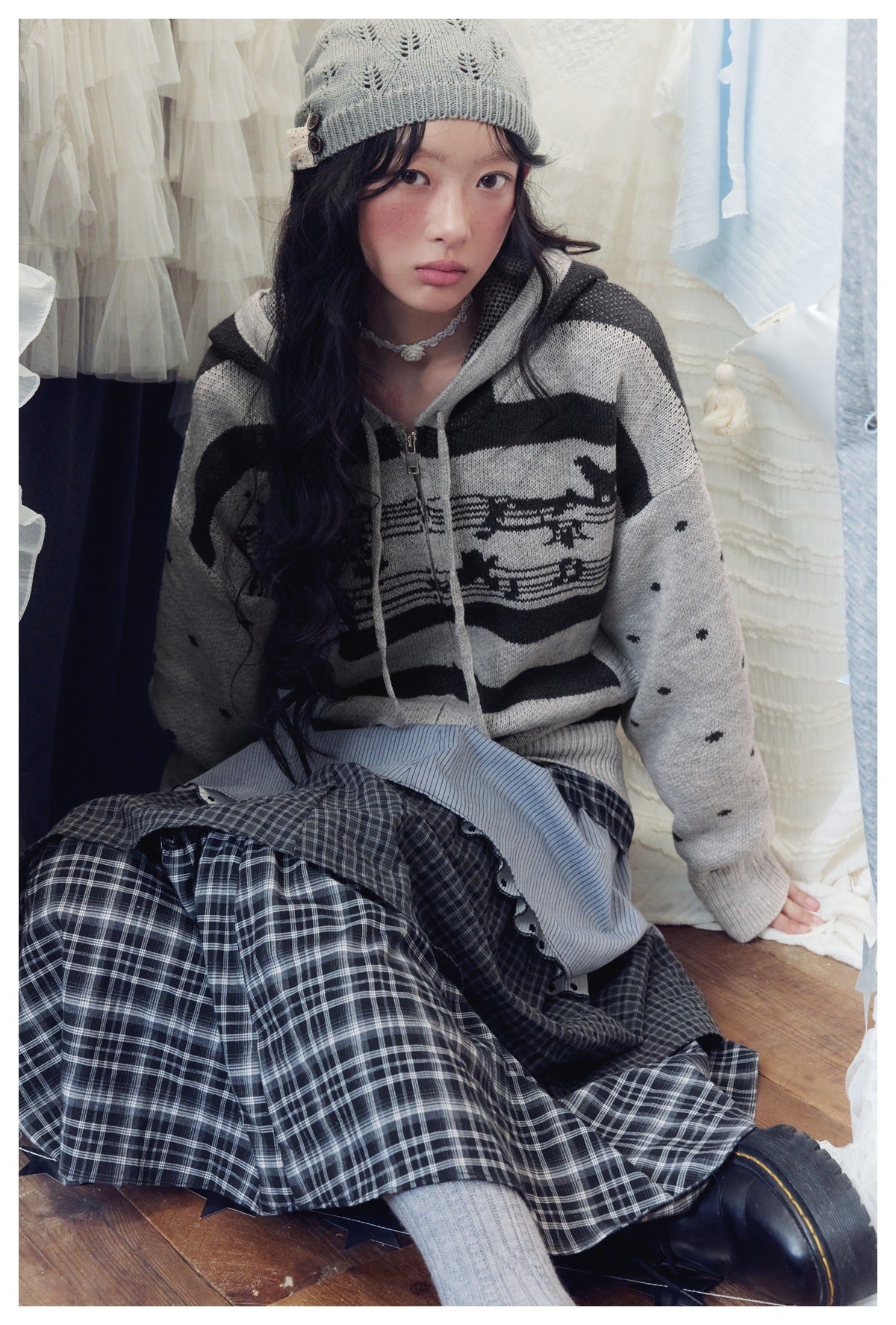 Model wearing a gray and black striped hooded sweater with dotted sleeves and a dark plaid skirt.