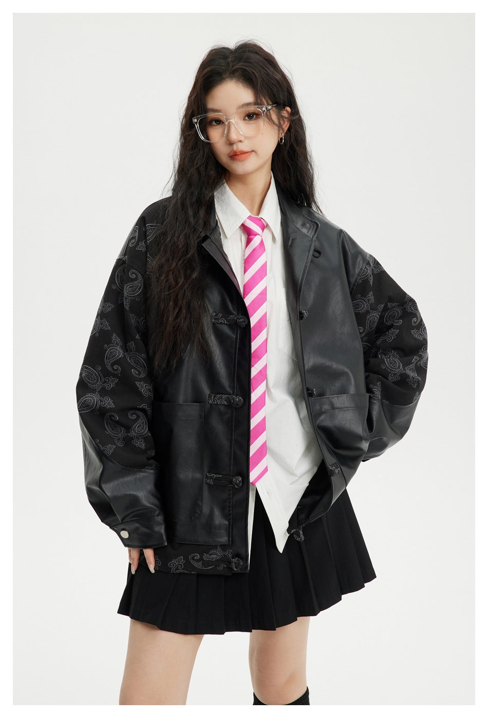 Front view of a model in an oversized black jacket with paisley sleeves, a white shirt, pink striped tie, and black pleated
