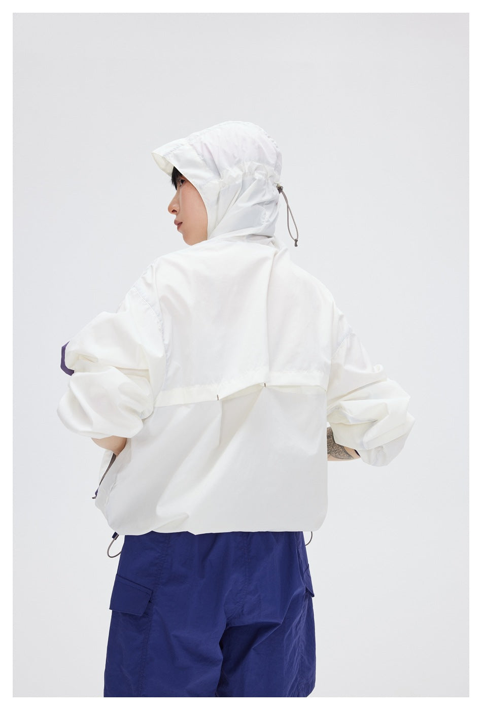 Rear view of a model wearing the white hooded jacket, showing its back panel and adjustable hood cord.