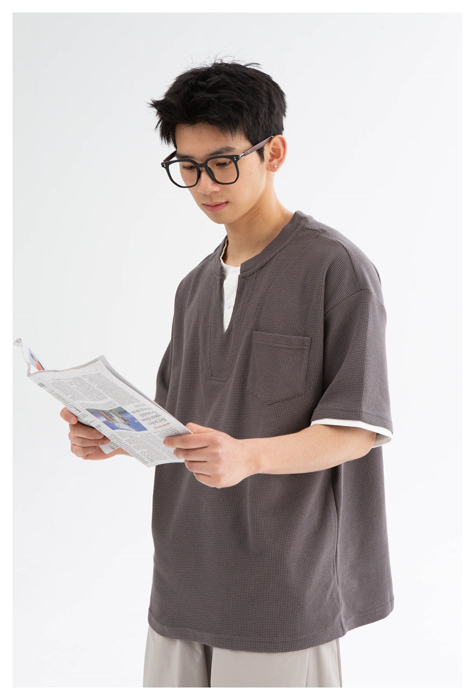 Man wearing a charcoal gray short-sleeve henley with a chest pocket and white trim, holding a newspaper.