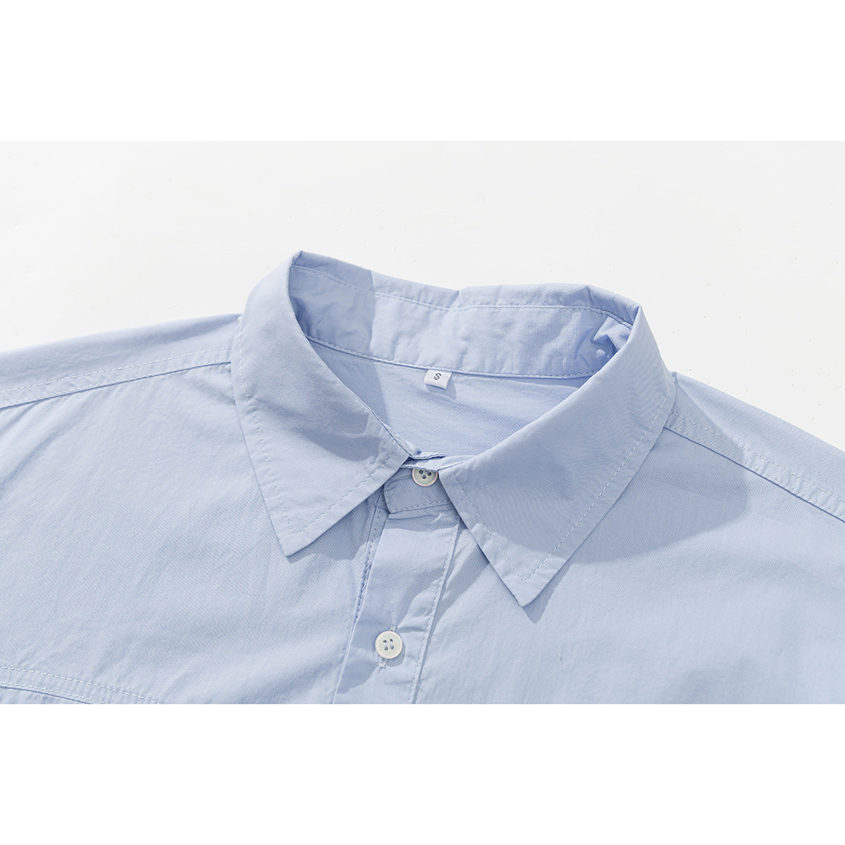 Close-up of a pale blue shirt's pointed collar, neckline, stitching, and front buttons.