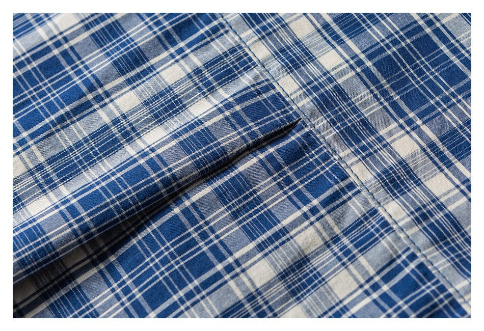 Close-up of a folded pocket edge and stitching on blue, white, and gray plaid shirt fabric.