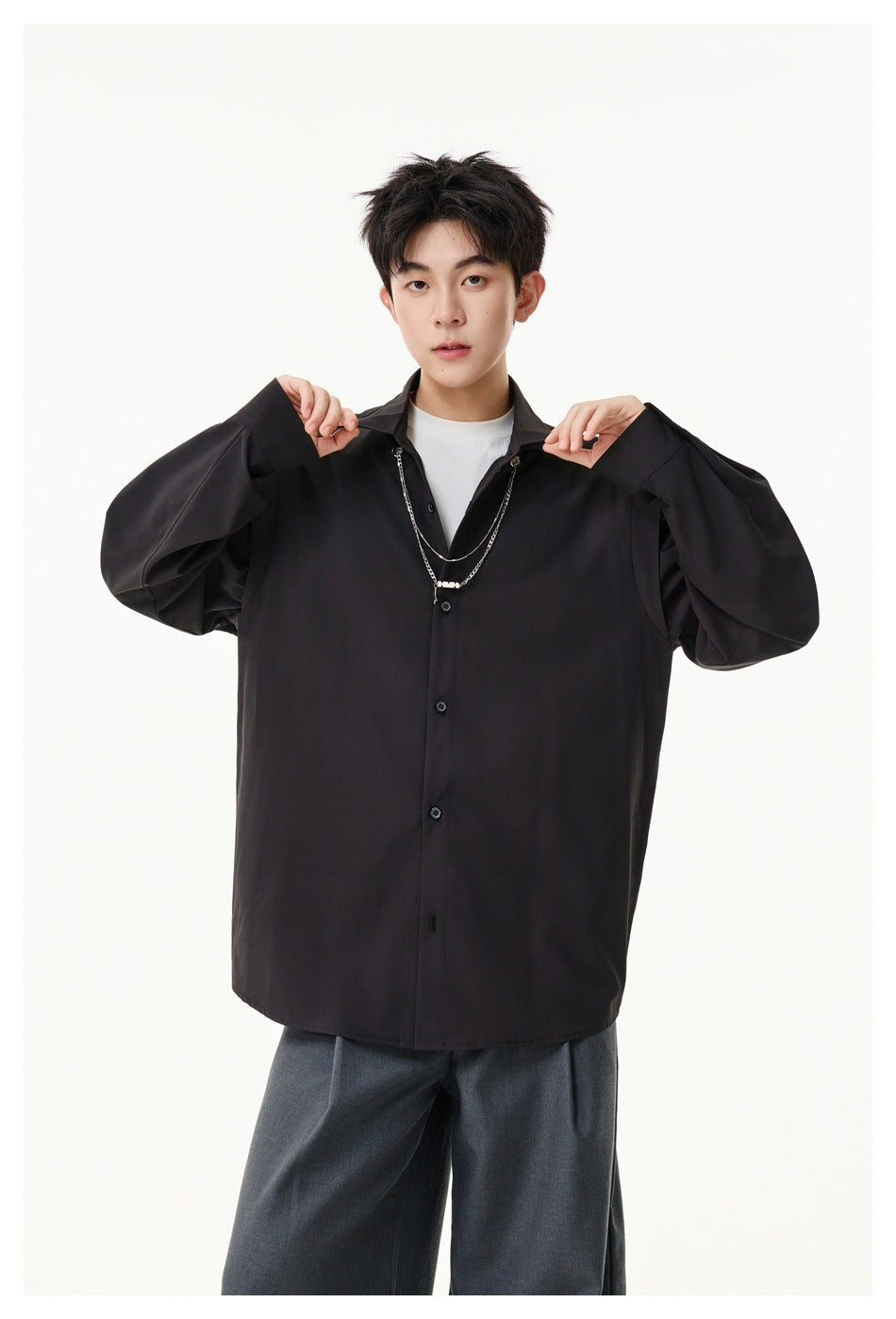 Model showing the front of a black button-front shirt with voluminous sleeves and a layered chain necklace.