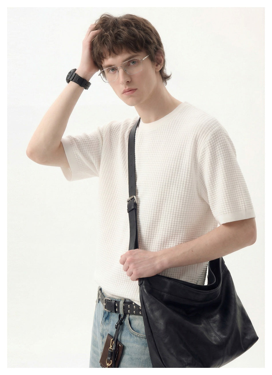 Close view of a model wearing a white textured short-sleeve shirt with a black shoulder bag.