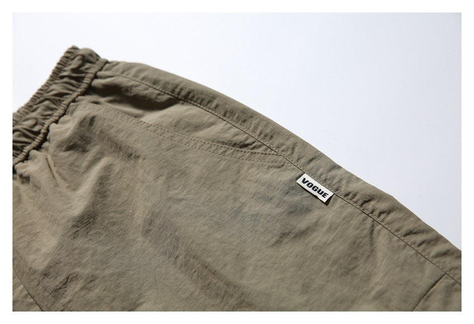 Close-up of olive-khaki shorts with a stitched pocket seam and a small sewn VOGUE label.