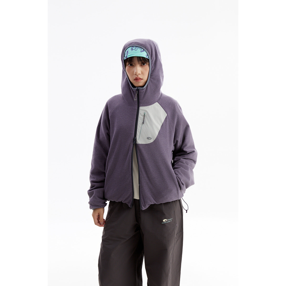 Model wearing a purple hooded zip jacket with a pale chest pocket panel and dark loose trousers.