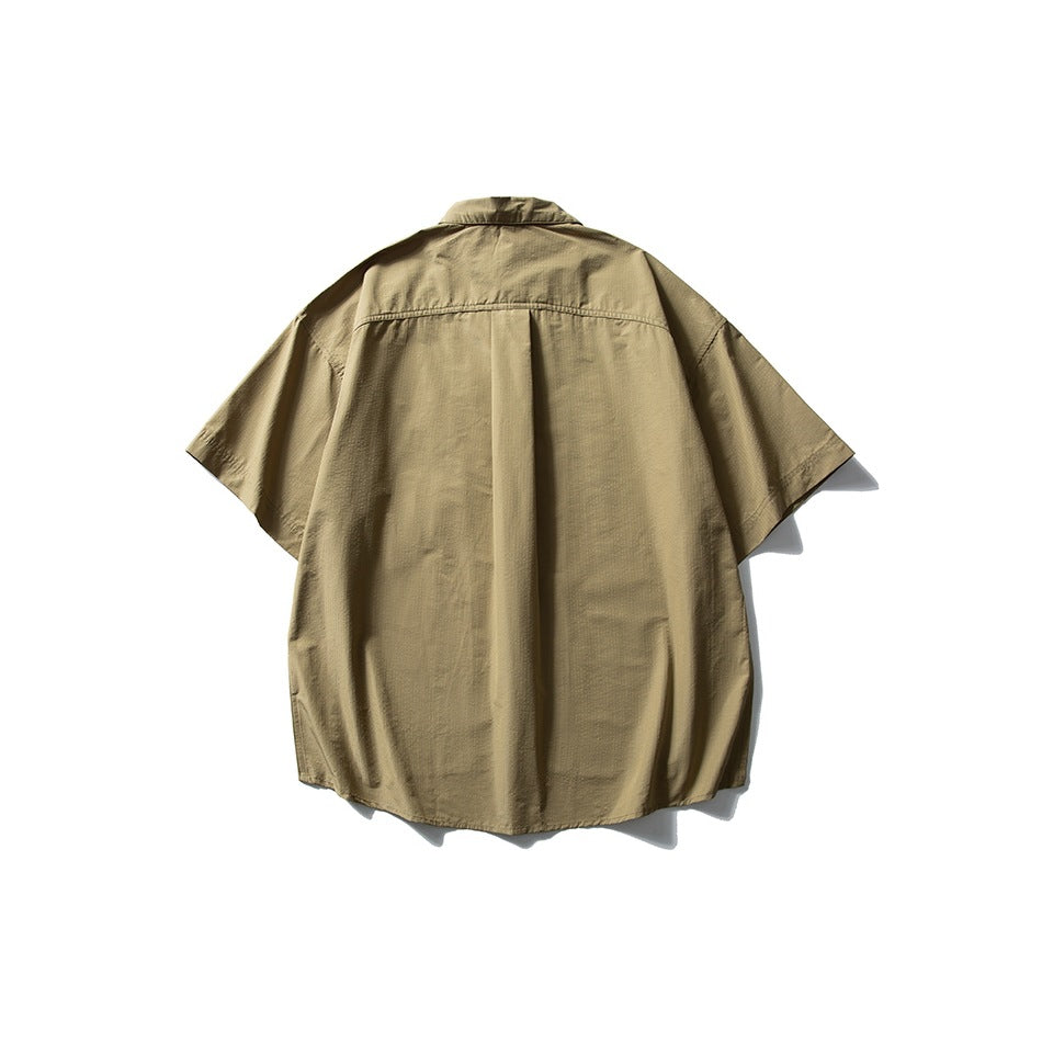Back view of a tan short-sleeve collared shirt with a center pleat and curved hem, displayed against white.