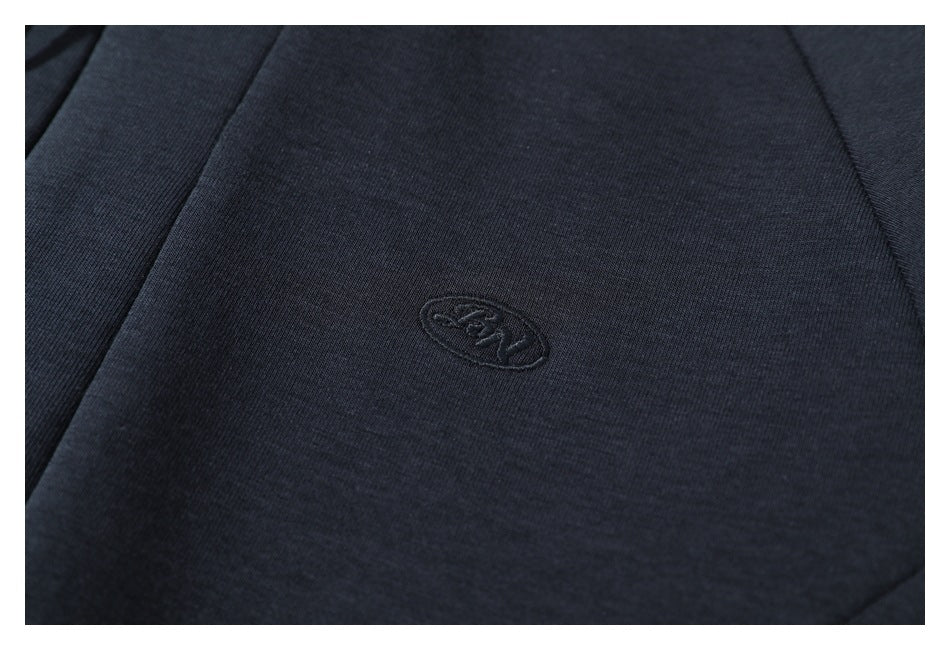 Close-up of a small tonal embroidered oval emblem on dark navy fabric.