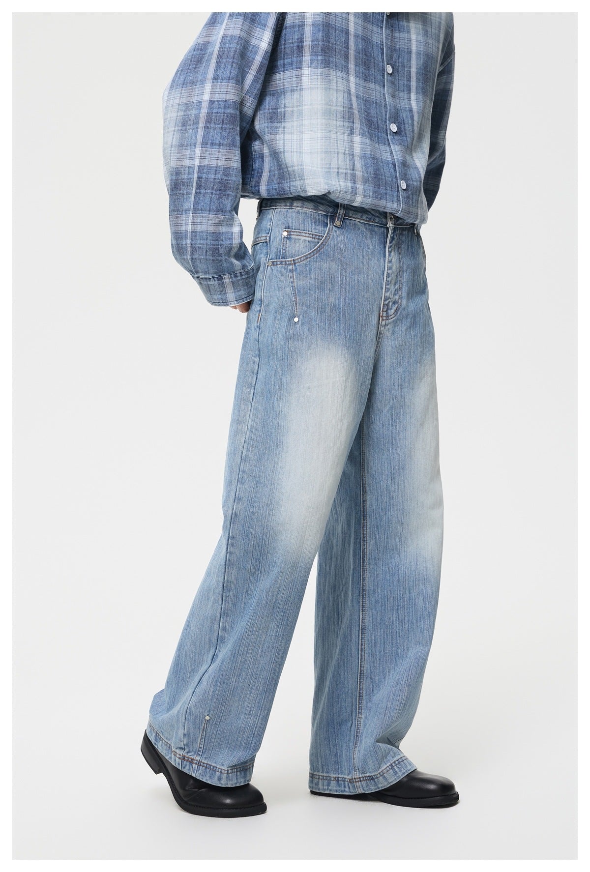 Side three-quarter view of wide-leg light blue jeans with faded knees, worn with plaid shirt and black boots
