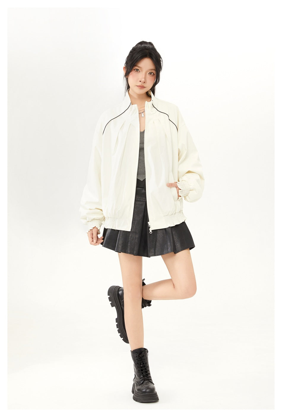 Model in an off-white stand-collar jacket with one hand in a pocket, styled with a black pleated skirt and boots