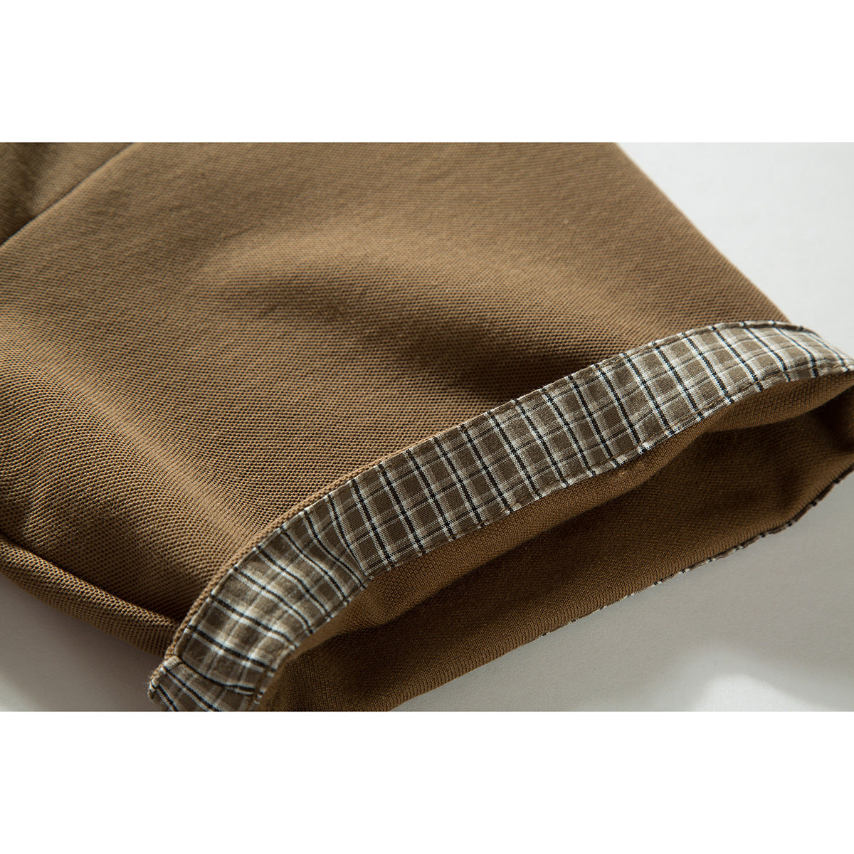Close-up of the tan polo shirt hem folded back to show its plaid inner trim.
