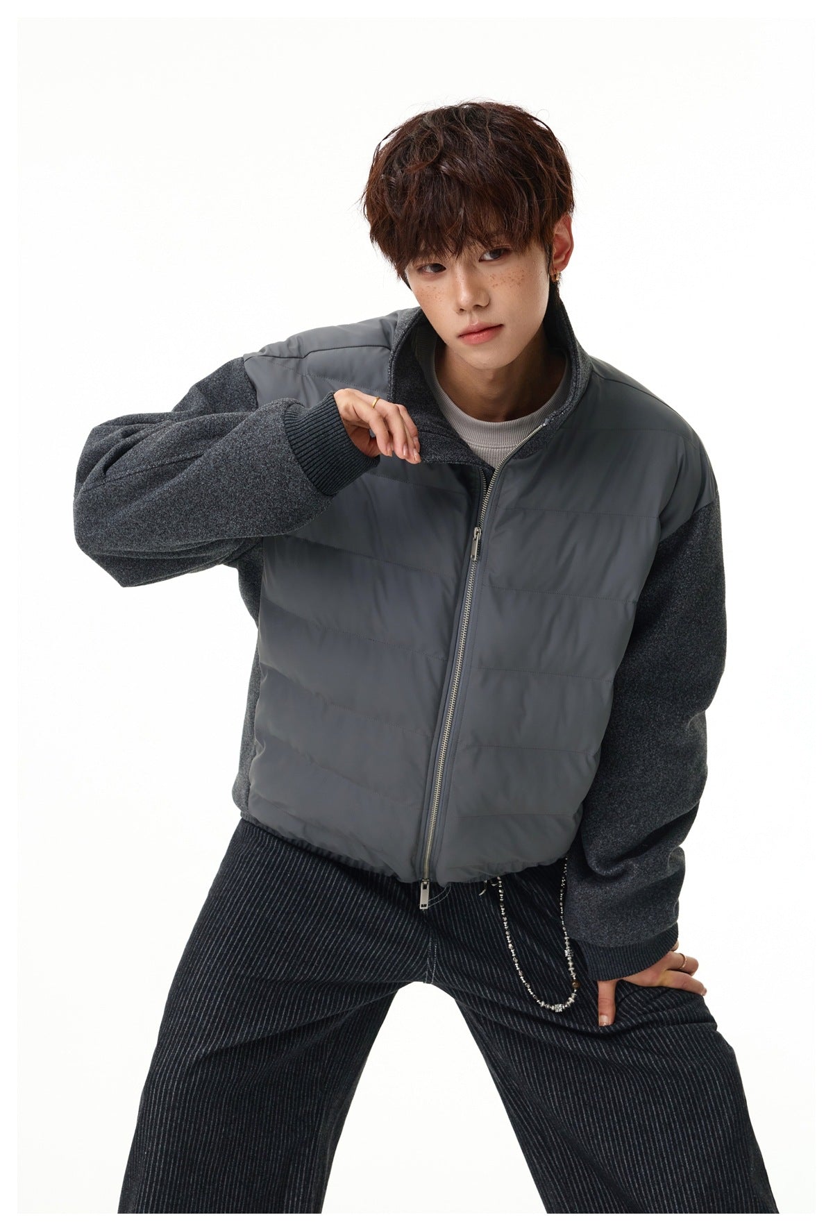 Model posing in a charcoal-gray quilted zip jacket with textured sleeves and a raised collar.