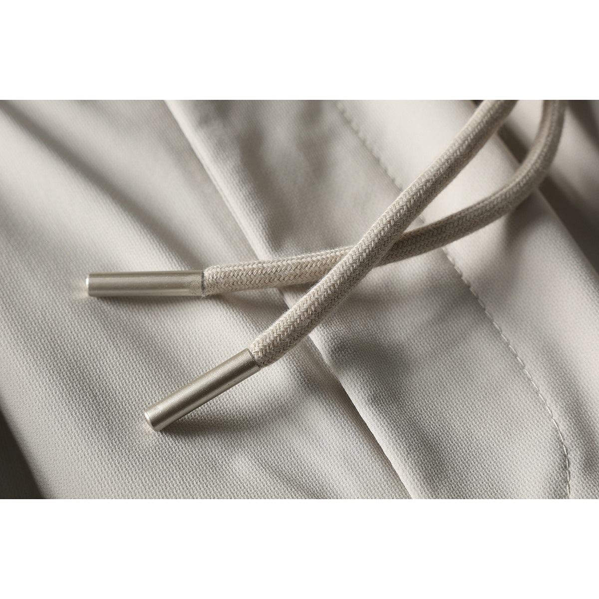 Close-up of braided drawstrings with metal tips against light beige shorts.