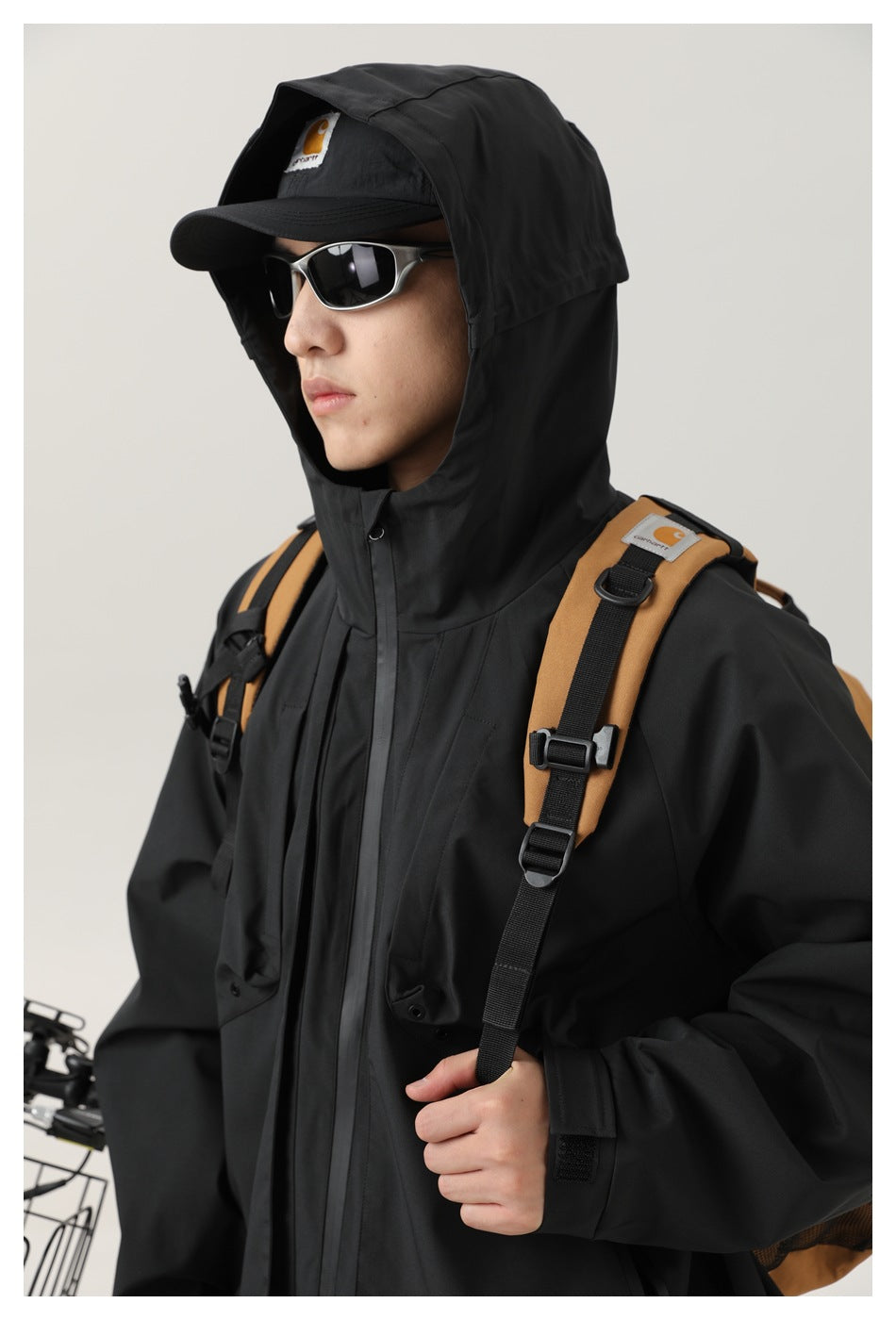 Close view of a model wearing a black hooded jacket with a front zipper and flap pockets.