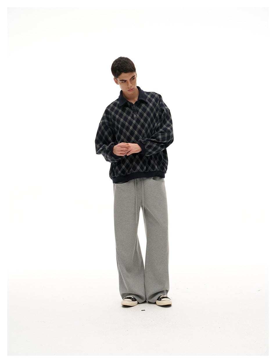 Model in a navy and gray diamond-plaid pullover and gray wide-leg pants, standing with hands together.