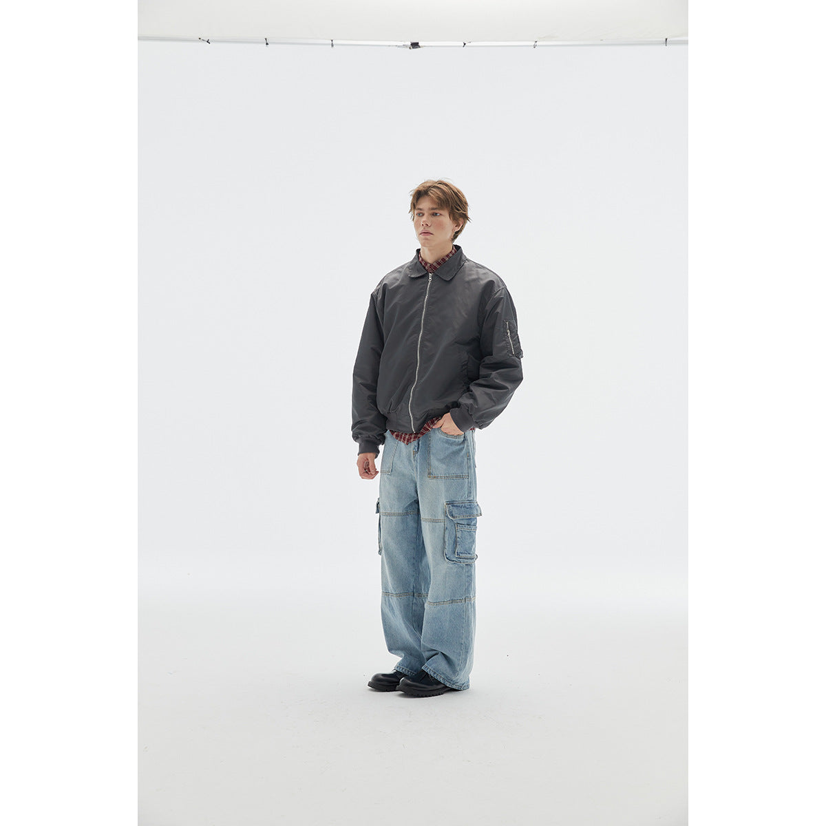 Model wearing a charcoal zip-front jacket with a collar and sleeve pocket, paired with light blue cargo jeans.