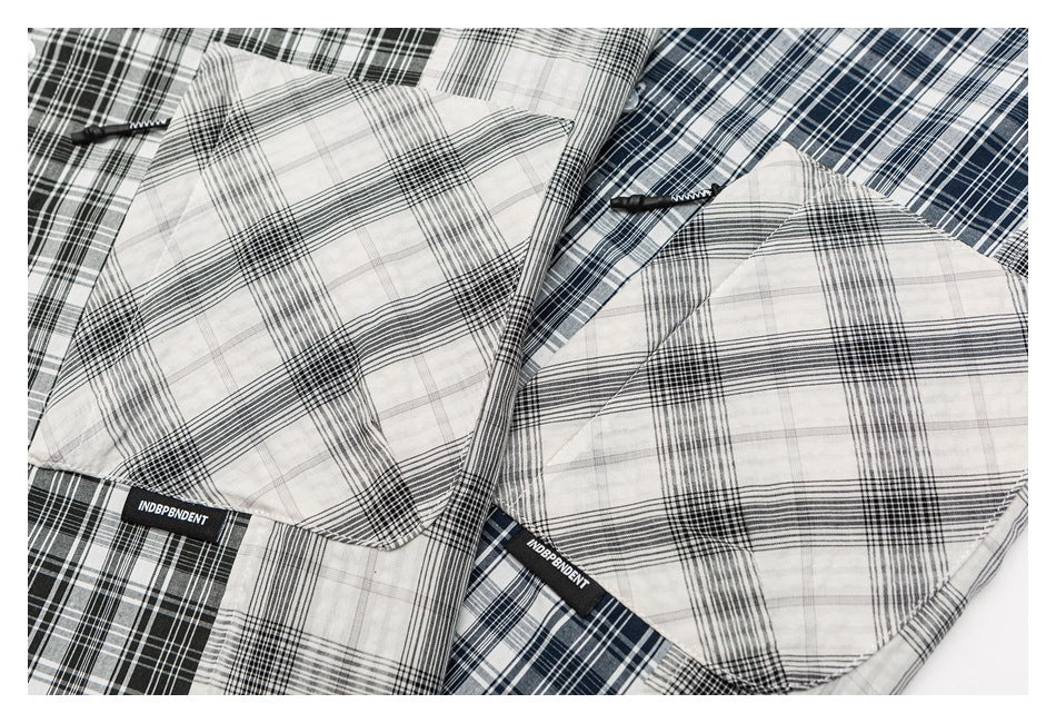 Close-up of overlapping black-and-white and navy plaid shirts, showing collars, fabric patterns, and sewn labels.