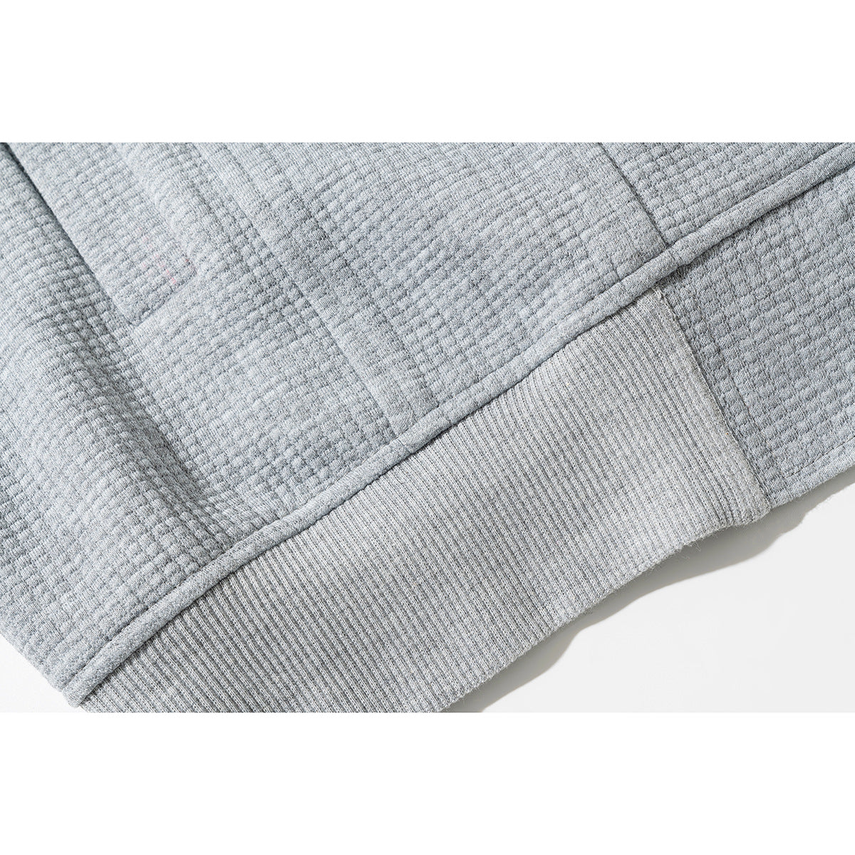 Close-up of a light gray jacket's textured fabric, stitched seam, and ribbed hem.